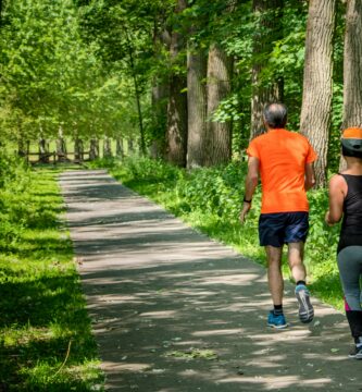 man in orange t-shirt and gray pants with blue shoes walking on pathway