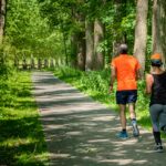 man in orange t-shirt and gray pants with blue shoes walking on pathway